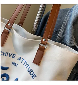 Detail of canvas tote bag with blue 3D embroidery and brown leather shoulder strap