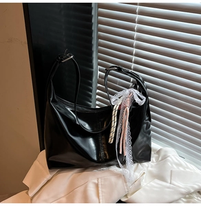 Detail of black glossy croissant bag with decorative lace and pink woven charm