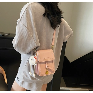 Detailed view of pink crossbody phone bag with fluffy white charm and metal logo