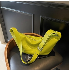 Detail of green hobo bag featuring wide strap with silver eyelets on a black chair