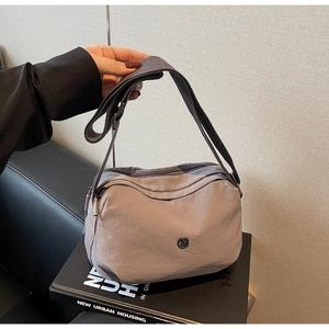 Détail d'un sac bandoulière en nylon gris avec plusieurs poches zippées et une bandoulière large