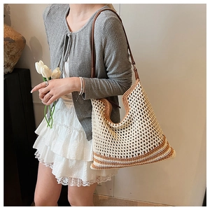 Detail of hollow woven straw tote bag with brown leather strap worn on shoulder