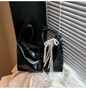 Detail of glossy black leather shoulder bag with delicate white lace and striped charm