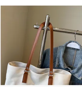 Detail of white canvas tote bag with brown leather handles and reinforced metal rivets