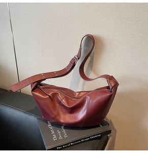 Close-up of burgundy crescent bag with litchi grain texture on decorative books