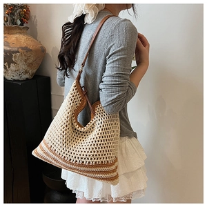 Detail of a woven hobo bag with beige and brown stripes and a leather shoulder strap