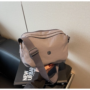 Détails de la bandoulière réglable et du logo en métal sur un sac bandoulière gris