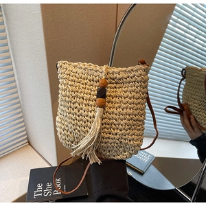 Dettaglio della borsa a secchiello in paglia beige con perline in legno e lunghe frange