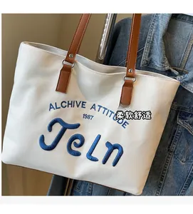 Detail of white canvas tote bag with blue letter embroidery and brown leather handles