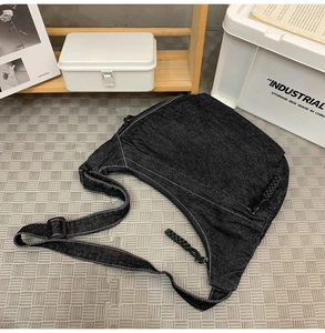 Detail of black canvas crossbody bag with white contrast stitching and plastic buckle closure