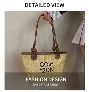 Detail of woven straw tote bag featuring brown leather straps and black embroidered logo