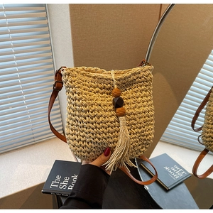 Dettaglio borsa a secchiello in paglia con texture intrecciata e nappa in legno