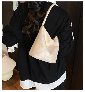 Close-up of cream bucket bag with yellow floral print worn over a black sweater