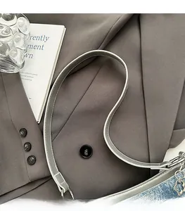 Detail of grey PU strap and blue denim bag with floral metal charm on book