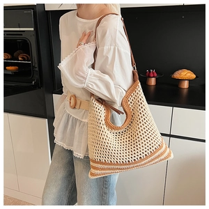 Close-up of beige woven hollow shoulder bag with brown leather strap on model