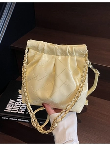 Sac seau plissé jaune clair avec matelassage et bandoulière chaîne sur bois