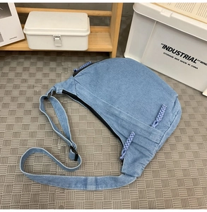 Detail of light blue denim crescent shoulder bag with purple braided rope zipper pull