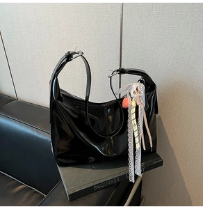 Detail of black glossy Hobo bag with white lace ribbon and a red heart pendant