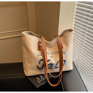 Detail of canvas tote bag with 1987 embroidery and brown handles in soft sunlight