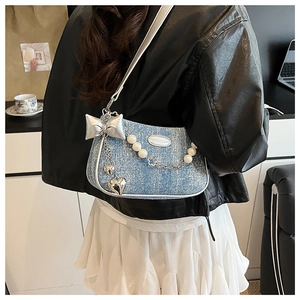 Détail du sac bandoulière en denim bleu avec nœuds argentés, perles et charms cœur
