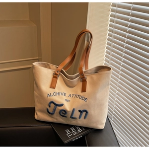 Detail of beige canvas tote bag with blue letter embroidery and brown leather handle