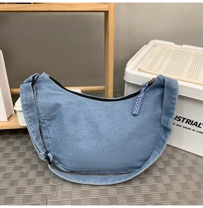 Detail of light blue denim hobo bag featuring a woven rope zipper pull and crescent shape