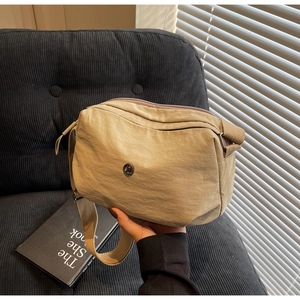 Détail d'un sac bandoulière en nylon kaki montrant la texture et le logo métallique