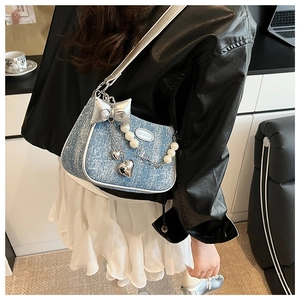 Détail du sac à bandoulière en denim bleu avec nœud argenté et chaîne de perles