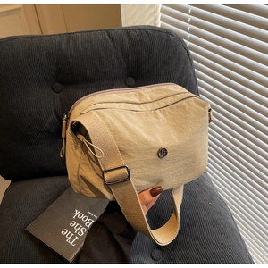 Détail d'un sac bandoulière en nylon beige avec logo en métal sur canapé gris