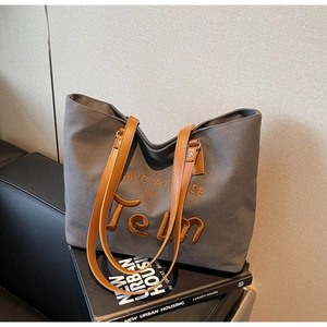 Detail of grey canvas tote bag with embroidered letters and brown leather handles