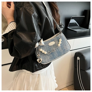 Détail du sac sous le bras en denim bleu clair avec chaîne de perles et nœud argenté