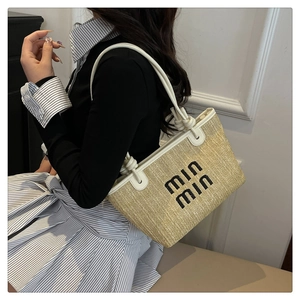 Detail of woven straw tote bag featuring black embroidered lettering and knotted white leather strap