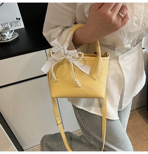 Detail of yellow bucket bag with lychee texture, logo embossing and pearl ribbon decor