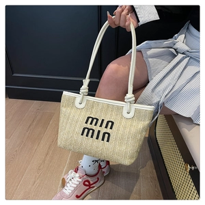 Close-up of beige woven straw tote with white leather handles and embroidered logo