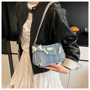 Detail of light blue denim crossbody bag featuring pearl chain and silver bow charms