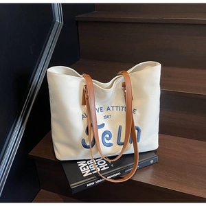 Detail of canvas tote bag with letter embroidery and leather straps on wooden steps