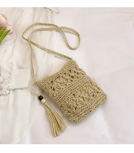 Detail of woven straw bucket bag with tassels and wooden beads on a white fabric surface