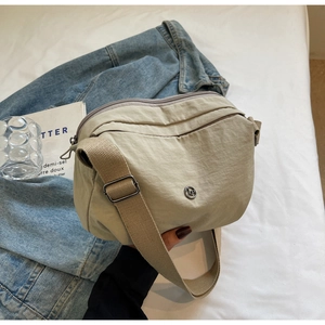 Détail du sac bandoulière en nylon beige avec zips multicouches et bandoulière large