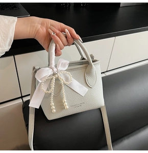 Detail of light green bucket bag with lychee grain leather, silk bow and pearl charm