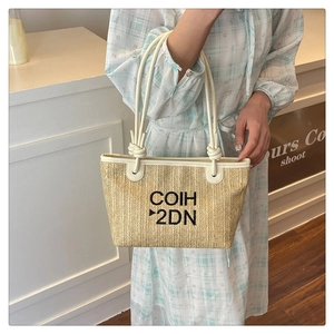 Detail of straw woven tote bag featuring cream faux leather trim and black embroidery