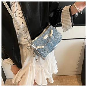 Detail of light blue denim crossbody bag with pearl chain and metallic bow charm