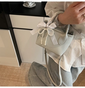 Detailed view of light grey lychee leather bucket bag with satin bow and pearl charm
