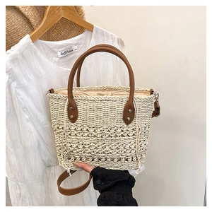 Detail of straw tote bag with brown leather handles and drawstring inner bag for beach