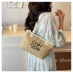 Detail of woven straw tote bag with white leather handles and large COIH 2DN print