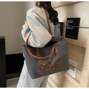 Detail of grey canvas tote bag featuring brown leather straps and orange letter embroidery
