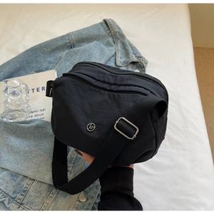 Détail du sac bandoulière en nylon noir avec plusieurs zips et boucles argentées