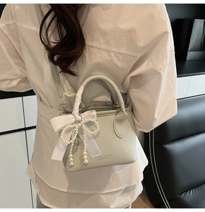 Detail of light green litchi grain bucket bag with pearl pendant and white ribbon bow