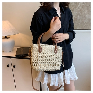 Close-up of beige woven straw bucket bag with brown leather handles and shoulder strap
