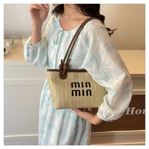 Detail of woven straw tote bag with brown leather handles and min min embroidery