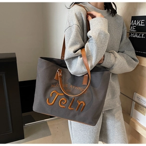 Detail view of canvas tote bag with embroidered orange lettering and brown leather handles